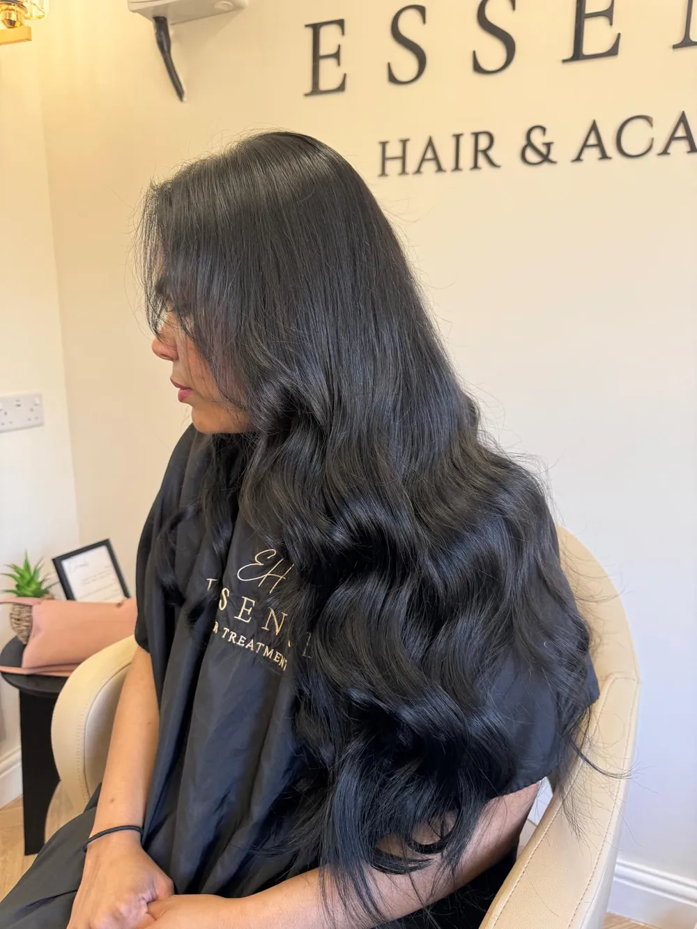 Long, voluminous black wavy hair extensions on a client in the Essence salon